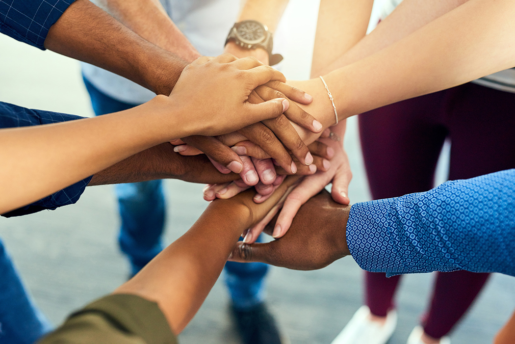 All together guys Shot of a group unrecognizable people putting their hands together in a huddle in side of a building